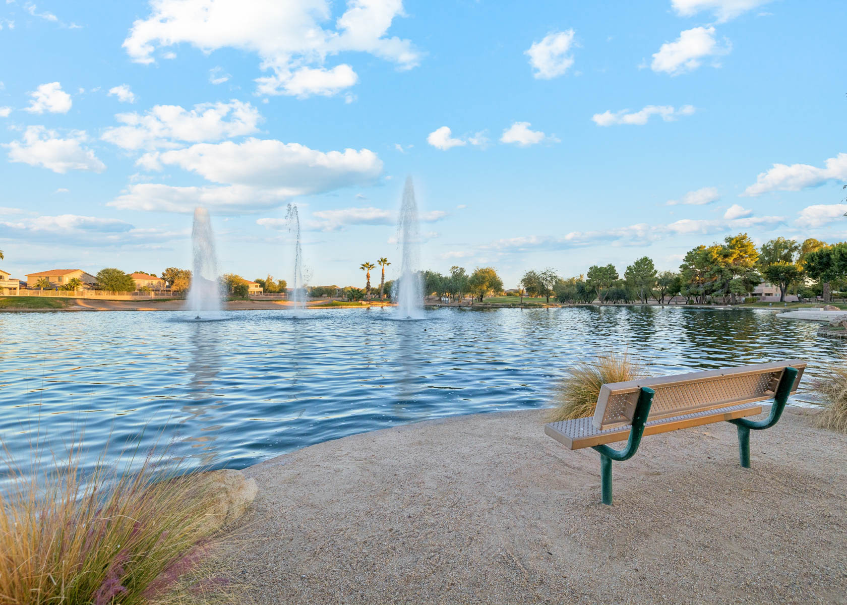 A bench next to a body of water with a fountain in the background.