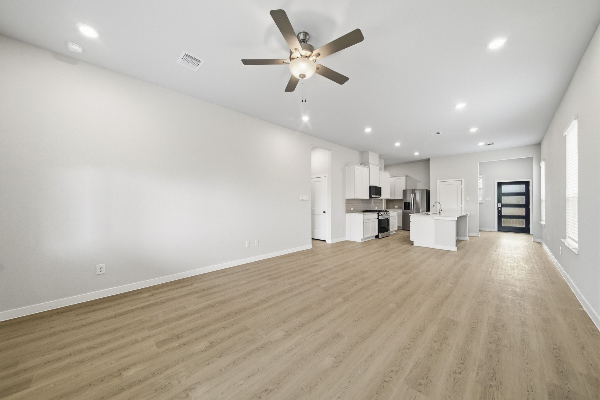 A large empty room with a ceiling fan and a wood floor.