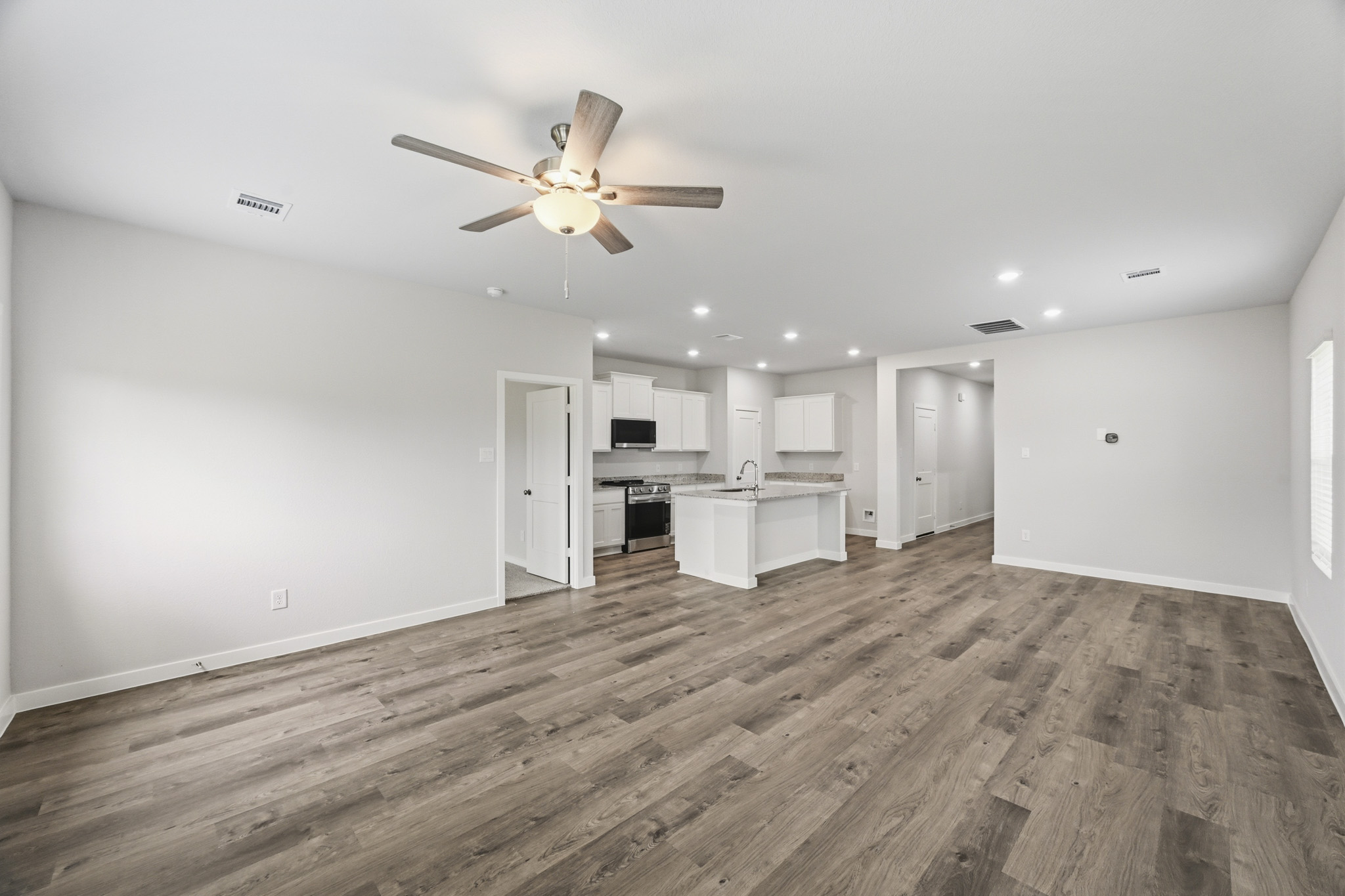 A large empty room with a ceiling fan and a wood floor.