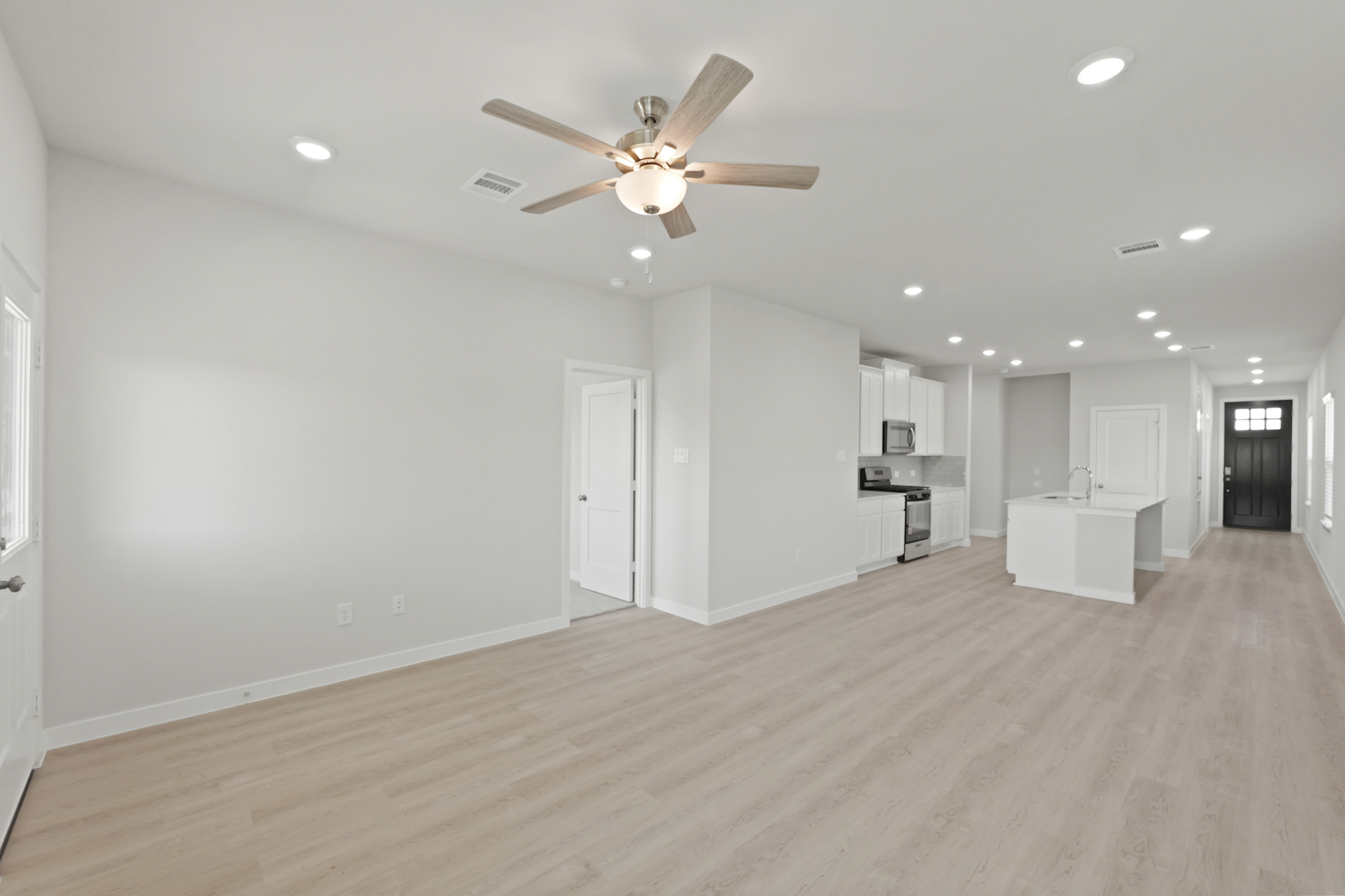 A large empty room with a ceiling fan and a wood floor.