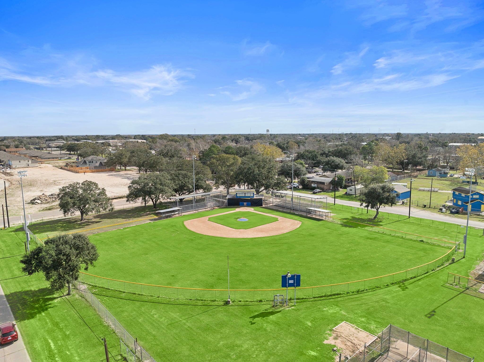 A large green field with a few trees and a few buildings.